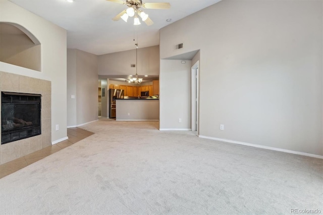 unfurnished living room featuring a tile fireplace, light carpet, ceiling fan with notable chandelier, and high vaulted ceiling