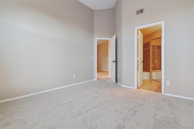 unfurnished bedroom featuring light colored carpet, a towering ceiling, and connected bathroom