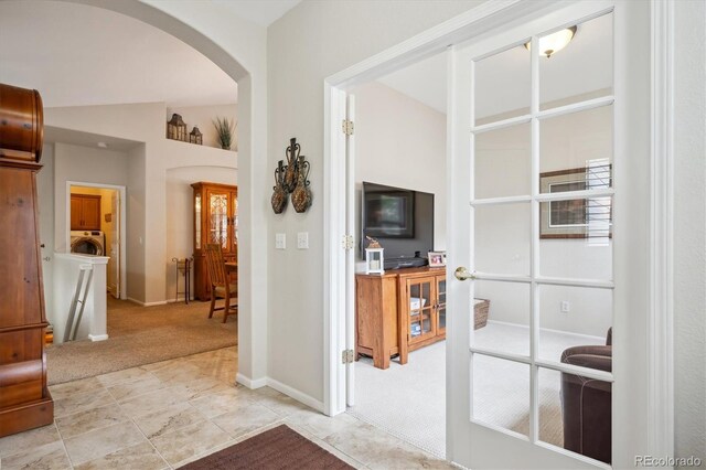 corridor with light carpet, arched walkways, washer / clothes dryer, baseboards, and lofted ceiling