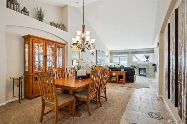 dining room with an inviting chandelier, high vaulted ceiling, baseboards, a glass covered fireplace, and light carpet