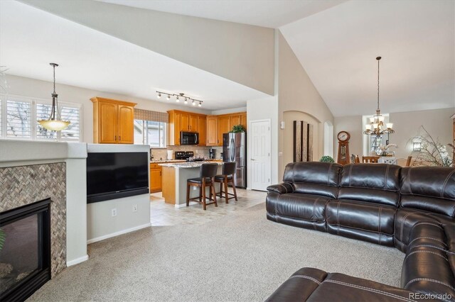 living area with light carpet, a fireplace, baseboards, a notable chandelier, and vaulted ceiling