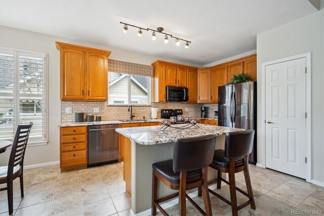 kitchen with a kitchen breakfast bar, backsplash, appliances with stainless steel finishes, a sink, and light stone counters