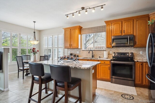 kitchen with light stone counters, appliances with stainless steel finishes, backsplash, and a breakfast bar area