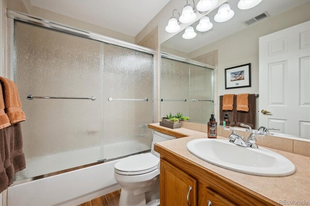 bathroom featuring visible vents, wood finished floors, vanity, toilet, and enclosed tub / shower combo