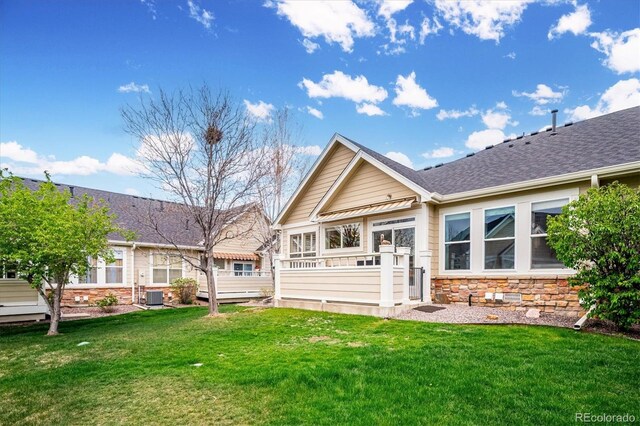 back of house with a yard, a shingled roof, cooling unit, and stone siding