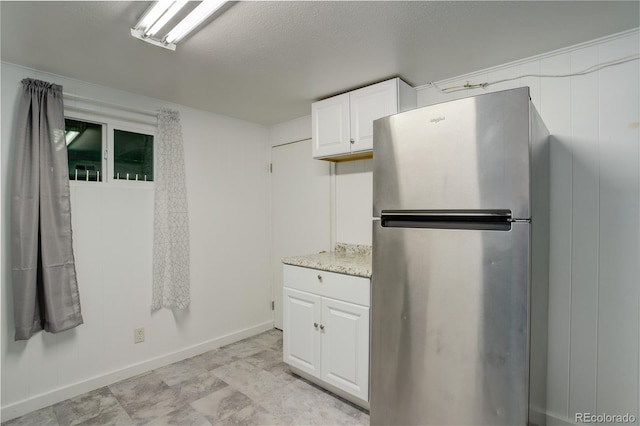 kitchen featuring light stone countertops, white cabinetry, a textured ceiling, and stainless steel fridge