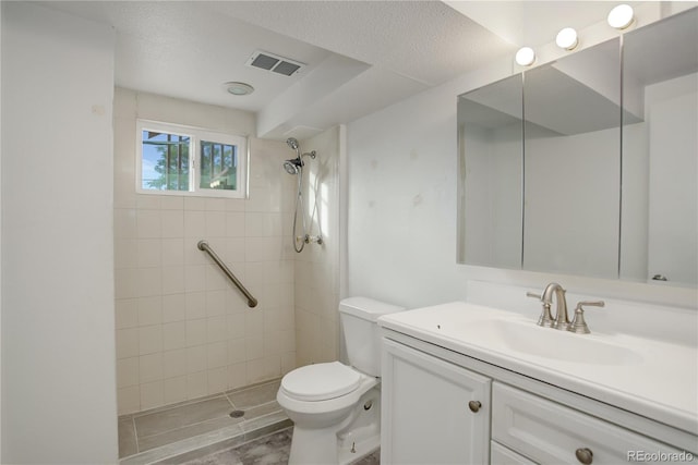 bathroom with a tile shower, vanity, a textured ceiling, and toilet