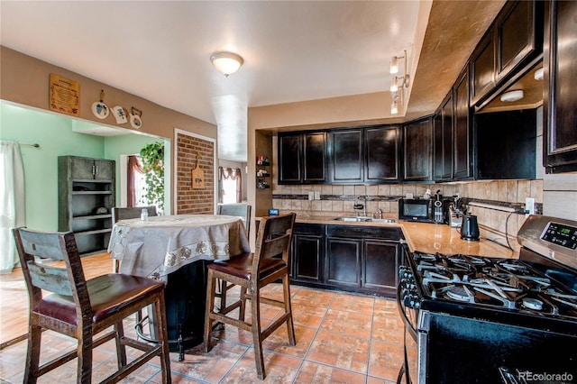 kitchen with stainless steel gas range oven, sink, rail lighting, tasteful backsplash, and light tile patterned flooring