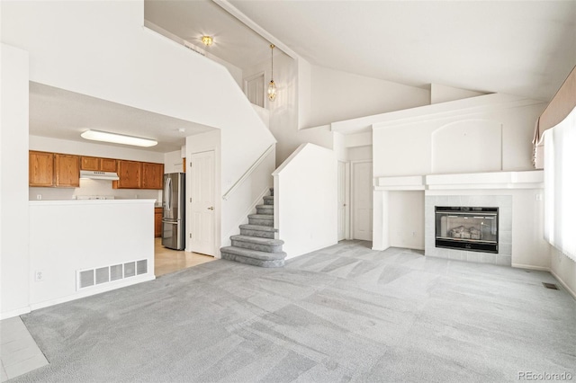 unfurnished living room featuring a tiled fireplace, high vaulted ceiling, and light colored carpet