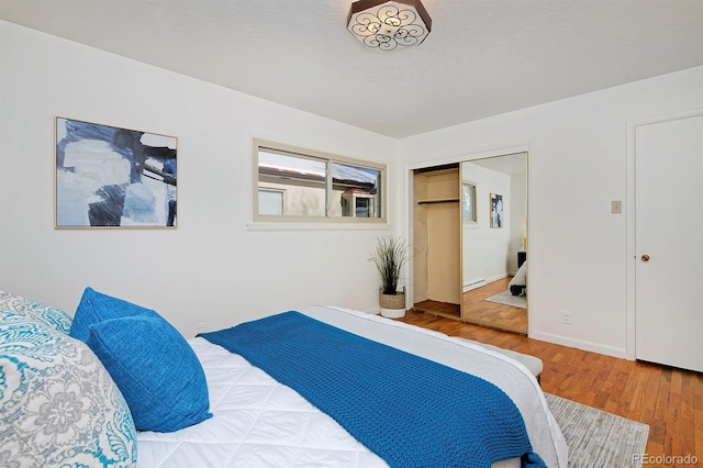 bedroom with a baseboard heating unit, hardwood / wood-style floors, and a closet