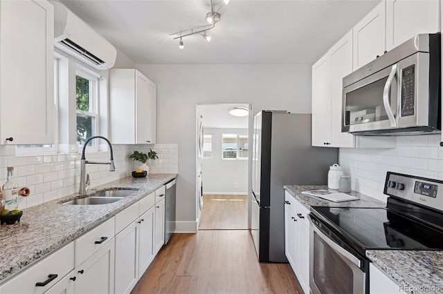 3976 S Washington St, Englewood, CO 80113 - kitchen with appliances with stainless steel finishes, a wall mounted AC, light wood finished floors, white cabinetry, and decorative backsplash
