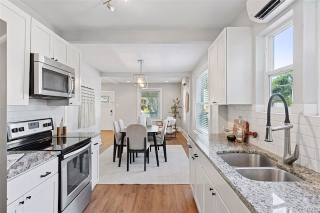 3976 S Washington St, Englewood, CO 80113 - kitchen with appliances with stainless steel finishes, a wall mounted air conditioner, light wood-style floors, white cabinets, and decorative backsplash