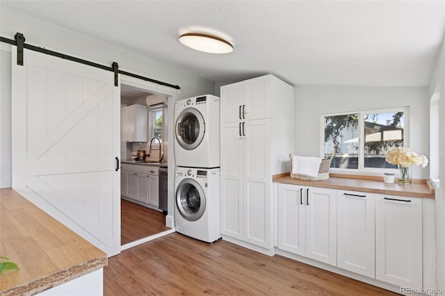 3976 S Washington St, Englewood, CO 80113 - laundry room featuring stacked washer / dryer, a barn door, light wood finished floors, cabinet space, and a wall mounted air conditioner