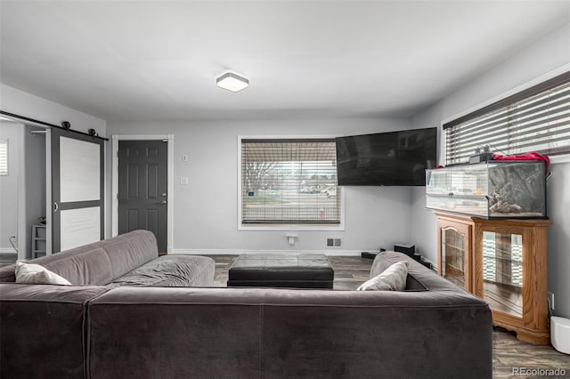 living room with a barn door, a healthy amount of sunlight, wood finished floors, and visible vents