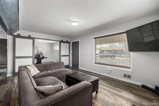 living room featuring a barn door, dark wood-type flooring, visible vents, and baseboards