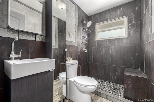 full bathroom featuring wood finished floors, toilet, tiled shower, and tile walls