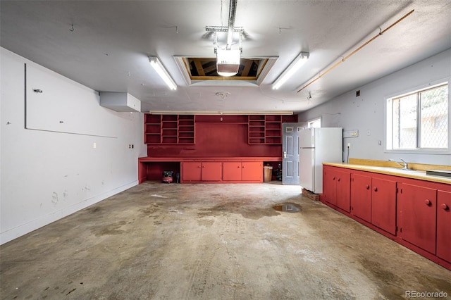 garage featuring baseboards, a sink, and freestanding refrigerator