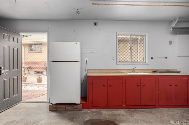 kitchen with red cabinetry, a sink, concrete flooring, freestanding refrigerator, and yellow cabinets