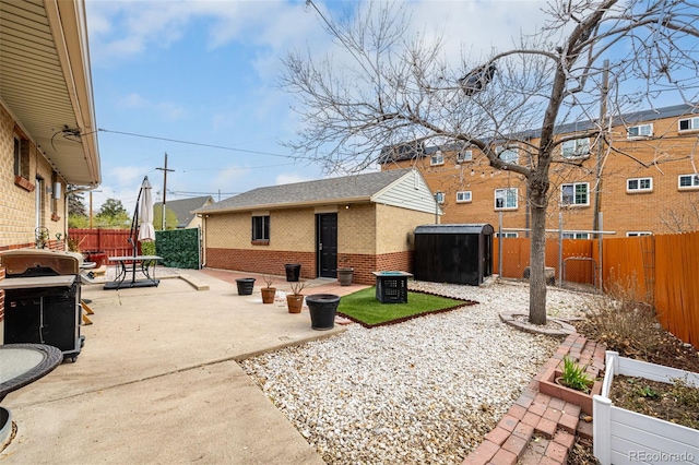 exterior space featuring a fenced backyard, roof with shingles, a patio area, an outdoor structure, and brick siding