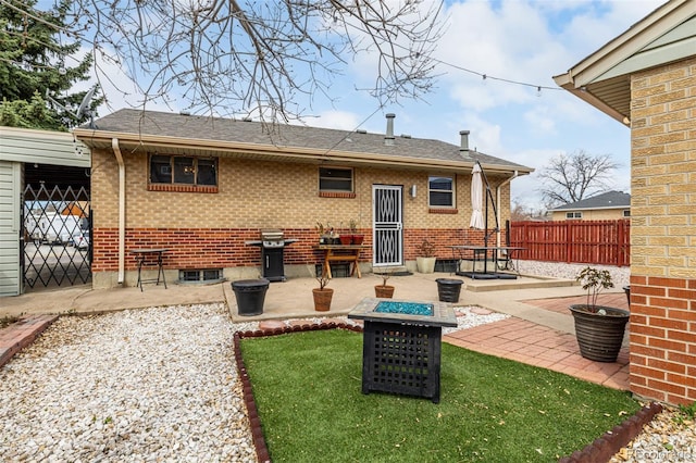 rear view of house featuring roof with shingles, fence, brick siding, a patio, and an outdoor fire pit
