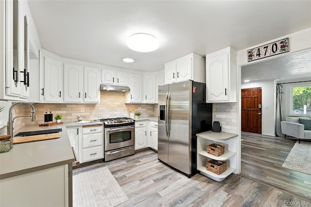 470 S Queen St, Lakewood, CO 80226 - kitchen with stainless steel appliances, under cabinet range hood, light wood-style floors, white cabinets, and decorative backsplash