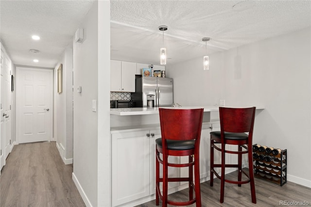 1160 S Monaco Pkwy Unit 6, Denver, CO 80224 - bar featuring stainless steel fridge, wood finished floors, a textured ceiling, tasteful backsplash, and hanging light fixtures