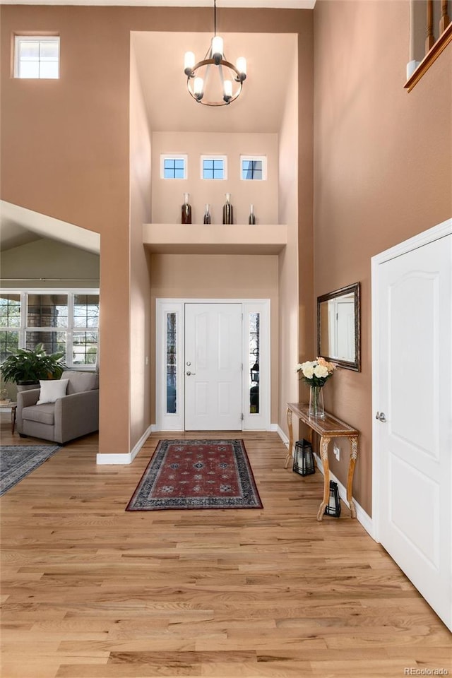 entryway with a chandelier, a towering ceiling, baseboards, and wood finished floors