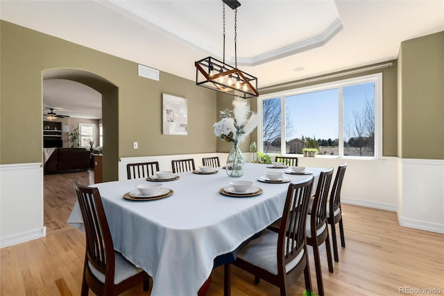 dining room with light wood-type flooring, crown molding, visible vents, a tray ceiling, and arched walkways