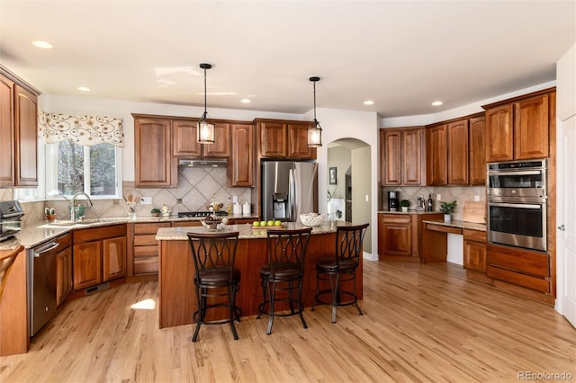 kitchen with arched walkways, a sink, light wood-type flooring, appliances with stainless steel finishes, and a kitchen island