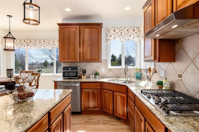 kitchen with under cabinet range hood, light stone countertops, light wood-style floors, appliances with stainless steel finishes, and a sink