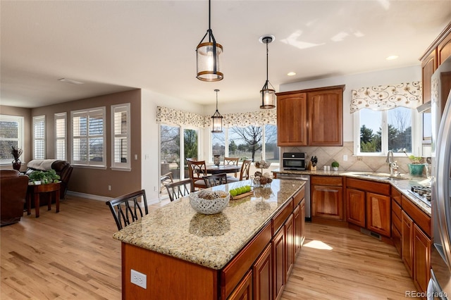 kitchen with light stone counters, open floor plan, light wood-style floors, decorative backsplash, and appliances with stainless steel finishes