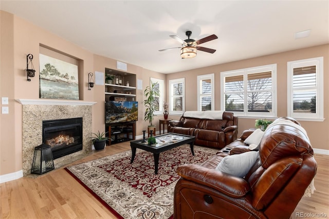 living room with a premium fireplace, wood finished floors, ceiling fan, and baseboards