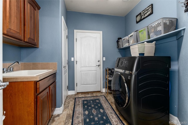clothes washing area featuring baseboards, a sink, and cabinet space