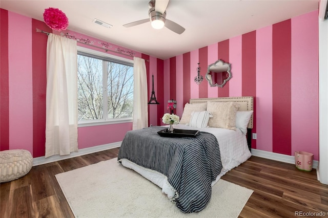bedroom featuring an accent wall, visible vents, wood finished floors, wallpapered walls, and baseboards