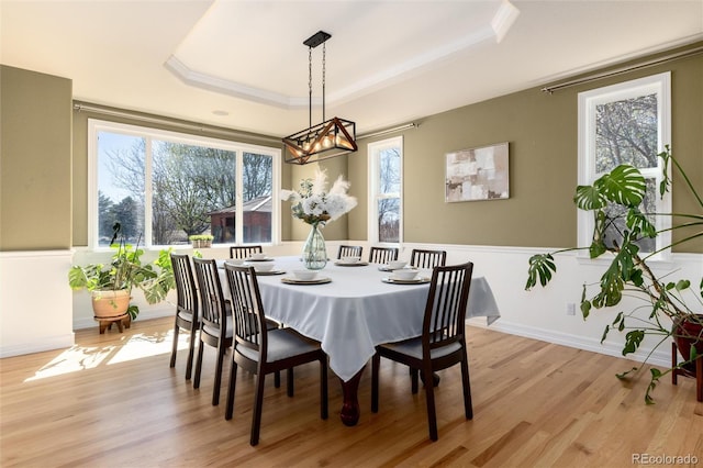 dining space with light wood-type flooring, a raised ceiling, a chandelier, and a healthy amount of sunlight
