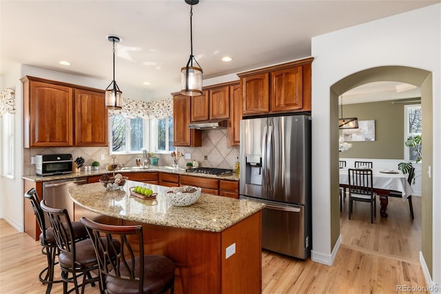 kitchen with light stone countertops, light wood-style flooring, arched walkways, a center island, and stainless steel appliances