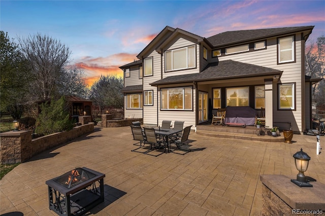 rear view of property featuring a patio area, a fire pit, outdoor dining area, and roof with shingles
