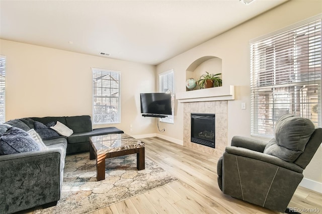 living room with light hardwood / wood-style floors, a healthy amount of sunlight, and a tiled fireplace