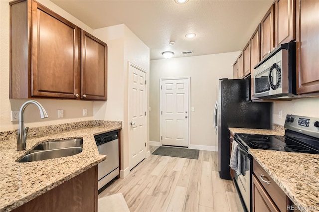 kitchen with sink, light stone countertops, a textured ceiling, appliances with stainless steel finishes, and light hardwood / wood-style floors