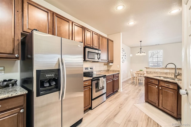 kitchen with stainless steel appliances, sink, pendant lighting, a notable chandelier, and light hardwood / wood-style floors