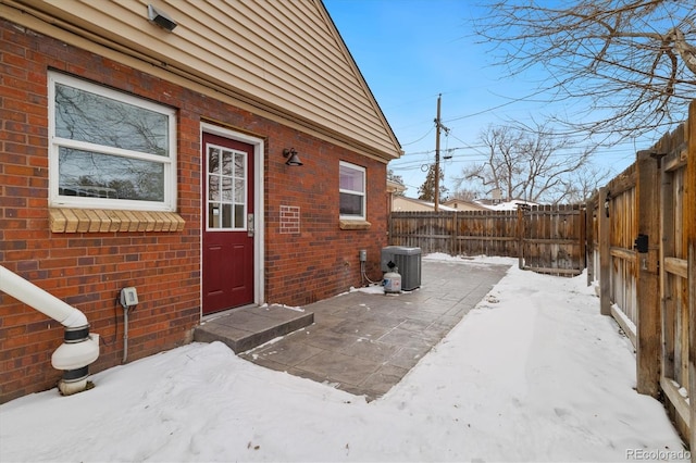 snow covered property entrance featuring central AC, brick siding, and fence