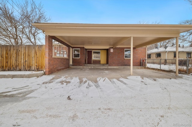 snow covered parking featuring a carport and fence