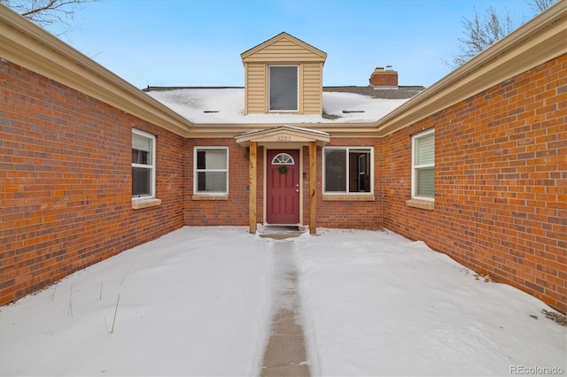 snow covered property entrance with brick siding and a chimney