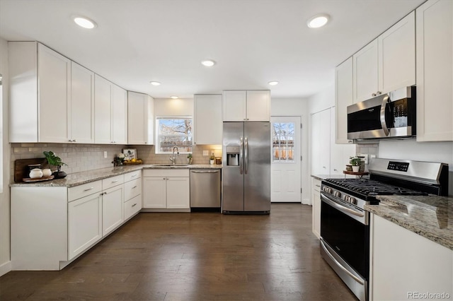 kitchen with light stone counters, dark wood-style flooring, appliances with stainless steel finishes, white cabinets, and a sink