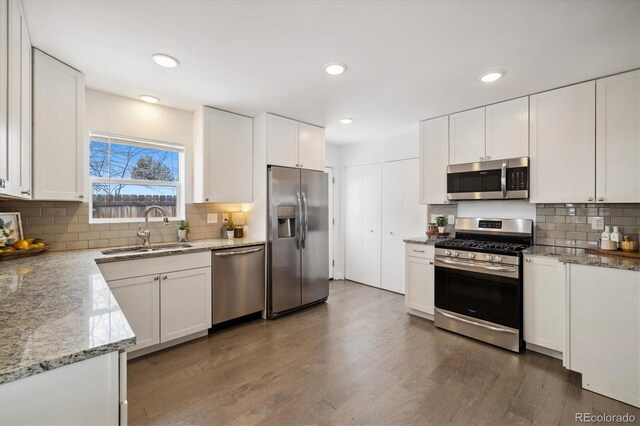 kitchen with light stone countertops, appliances with stainless steel finishes, white cabinets, and a sink