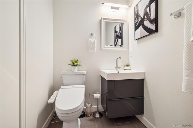 half bath with toilet, baseboards, and vanity