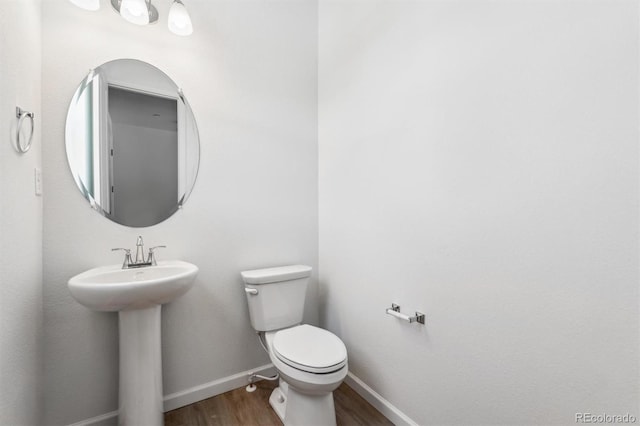 half bath with toilet, wood finished floors, baseboards, and a sink