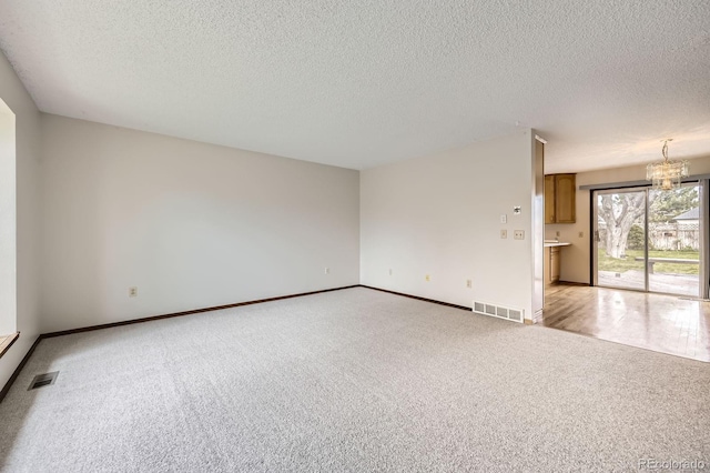 spare room featuring a textured ceiling, baseboards, visible vents, and light colored carpet