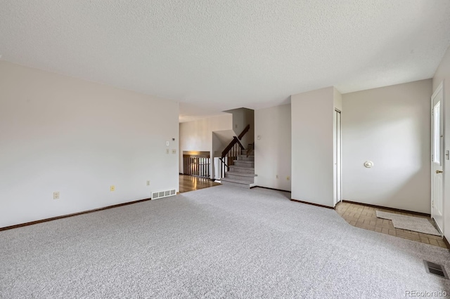 unfurnished living room with a textured ceiling, visible vents, stairway, and carpet floors