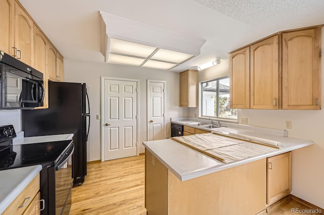 kitchen featuring a peninsula, light brown cabinets, black appliances, and a sink